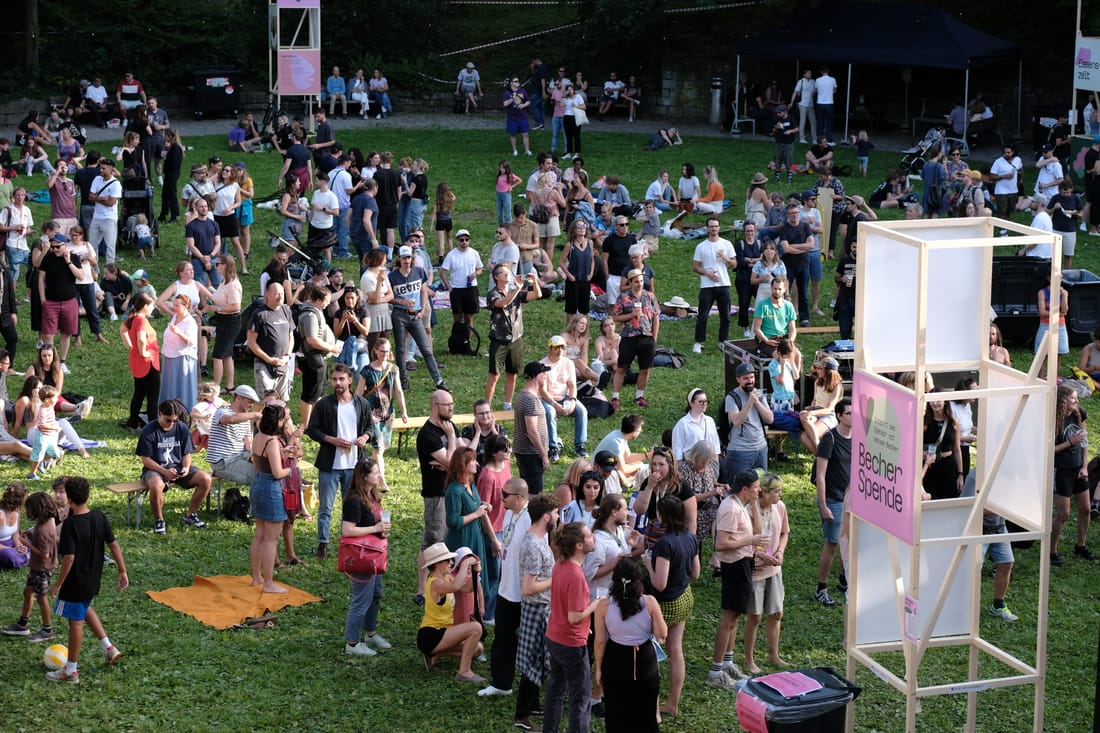 Publikum auf der Wiese im Bederpark beim Openair Enge, dazwischen ein Infoturm